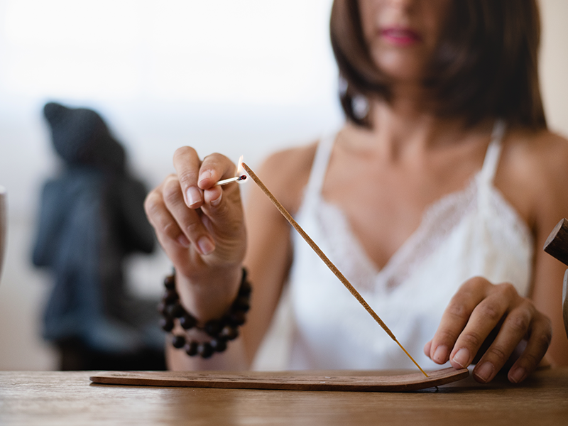 cerca-de-las-manos-de-la-mujer-quemando-un-palo-de-incienso-en-su-sala-de-estar-mujer-meditando-en-atmosfera-budista-durante-el-aislamiento-en-el-hogar