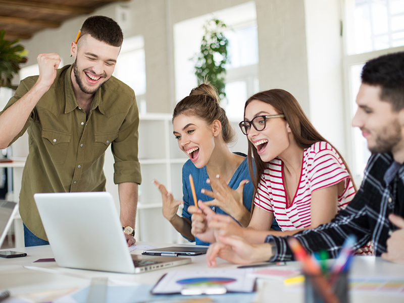 jovenes-empresarios-emotivos-trabajando-juntos-con-alegria-en-una-laptop-grupo-de-hombres-y-mujeres-que-se-rien-pasando-tiempo-en-el-trabajo-en-una-oficina-mo