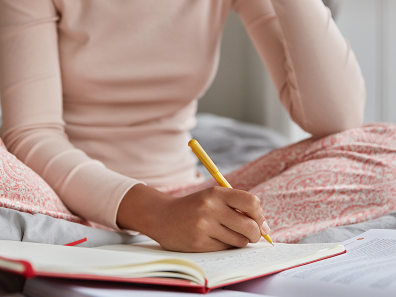 mujer-irreconocible-vestida-con-ropa-de-dormir-informal-escribe-en-un-cuaderno-tiene-inspiracion-para-estudiar