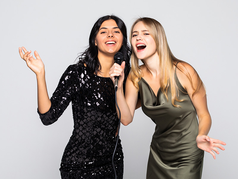dos-chicas-sensuales-cantando-con-microfono-aislado-en-pared-blanca