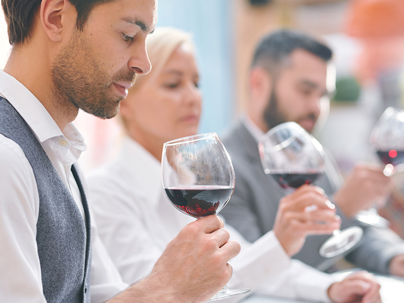 joven-experto-en-bodega-elegante-o-enologo-mirando-vino-tinto-en-copa-mientras-evalua-su-color-y-olor