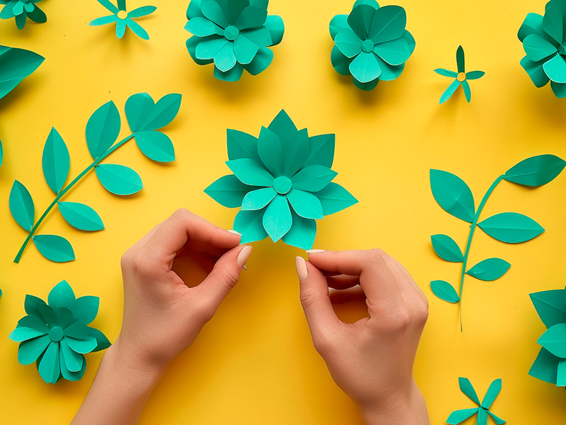 las-manos-de-las-mujeres-elaboran-flores-de-papel-coloridas-sobre-un-fondo-amarillo