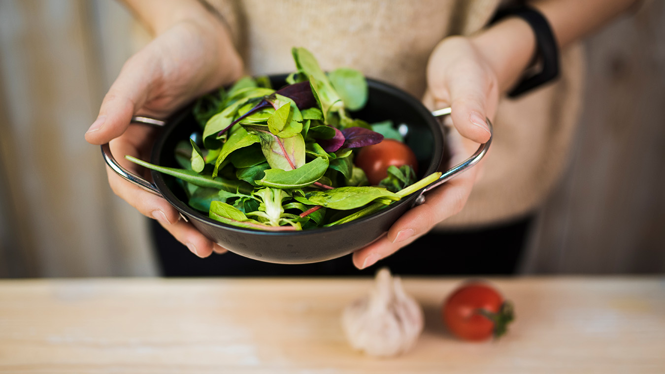 mediados-de-seccion-de-una-mujer-con-ensalada-de-verduras-frescas-en-un-recipiente-sobre-una-mesa-de-madera-con-ajo-y-tomate