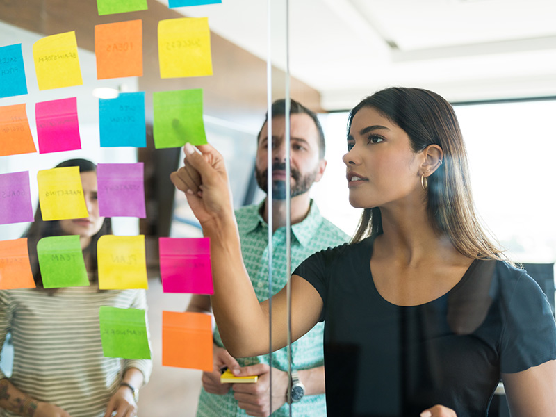 mujer-joven-gerente-discutiendo-sobre-una-nota-adhesiva-con-companeros-de-trabajo-en-una-reunion-de-oficina