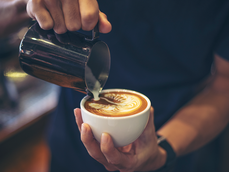 primer-plano-de-manos-barista-hacer-cafe-con-leche-arte-pintura