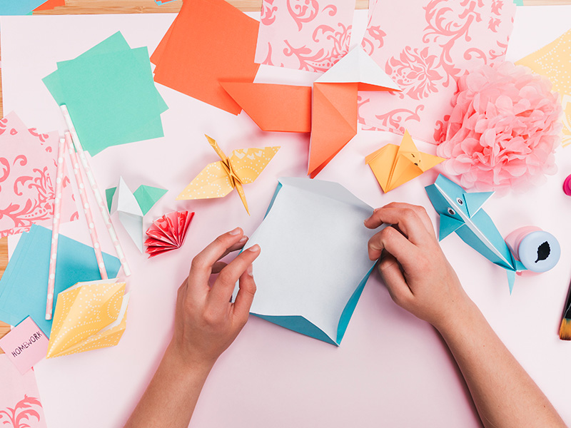 vista-elevada-de-la-mano-humana-que-hace-el-arte-del-papel-del-origami-en-la-tabla-de-madera